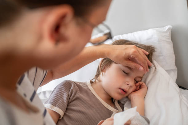 istock Sick child sleeping at home in bed with flu, cold, coronavirus, bronchitis or pneumonia, virus or infection and his mother touching his forehead checking temperature 1920296457