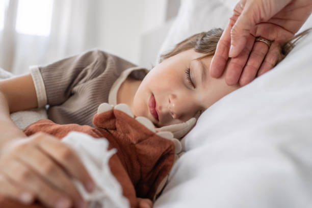Sick child sleeping at home in bed with flu, cold, covid, bronchitis or pneumonia, virus or infection and his mother's hand touching his forehead checking temperature Little boy ill at home with a virus or infectious disease fever stock pictures, royalty-free photos & images