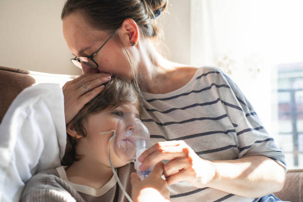 Sick child with mother makes inhalation with nebulizer at home in bed with flu, cold, covid, bronchitis or pneumonia, virus or infection stock photo