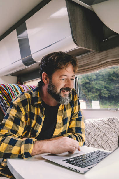 istock Alternative nomad lifestyle office workstation people. Man working on laptop computer inside luxury van during vacation or alternative digital lifestyle. People working online everywhere 1920315431