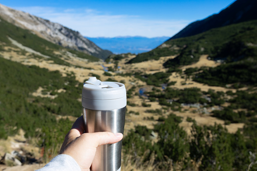 holding thermo bottle with drink in mountains
