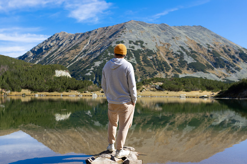 Young man standing near the lake and mountain and enjoying view of nature. High quality photo