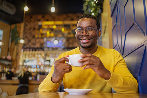 Happy black man drinking his morning coffee and relaxing in cafe