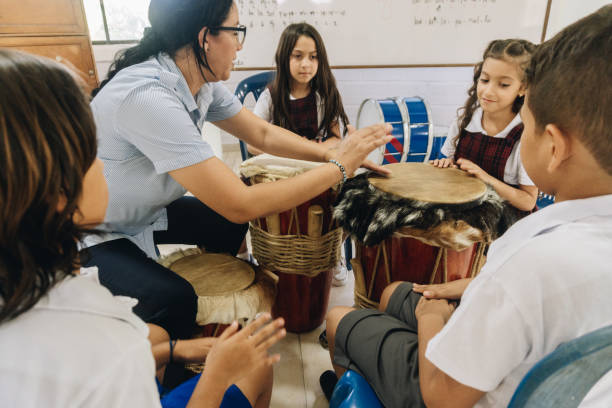 Mature teacher teaching child students to play drum in school classroom
