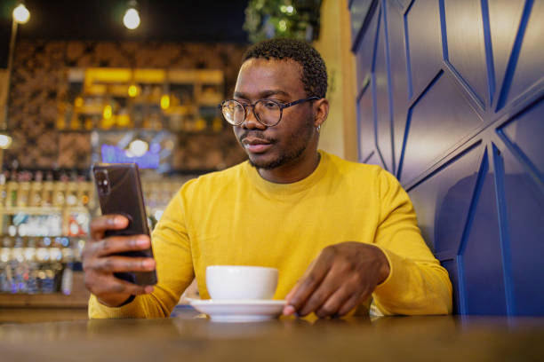 istock Shot of a young black man using a phone and having coffee in a cafeteria 1920370185
