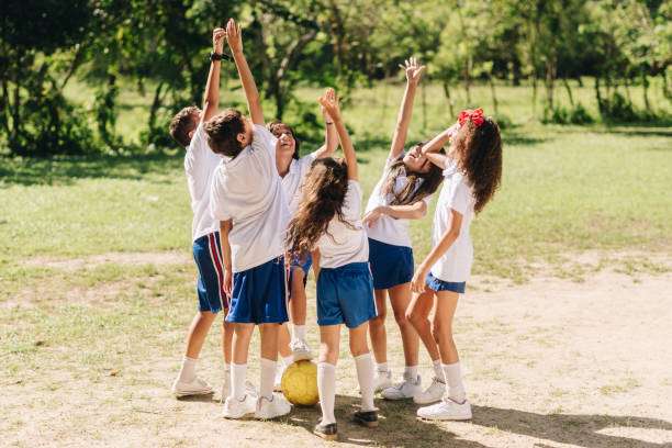 A multi-ethnic group of elementary age children are cheering and lifting a teammate in the air after winning a game.