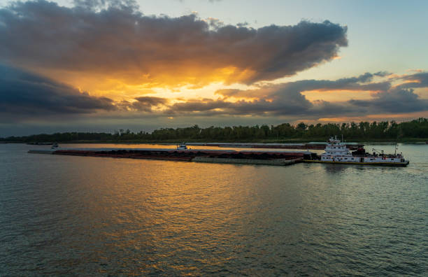 Dramatic sunset over river barge carrying coal down the Mississippi river in Baton Rouge Louisiana looking towards Port Allen