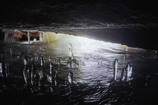 An underground cave covered with ice, ice stalagmites growing in the cave, frozen water underground, light at the end of the exit. High quality photo