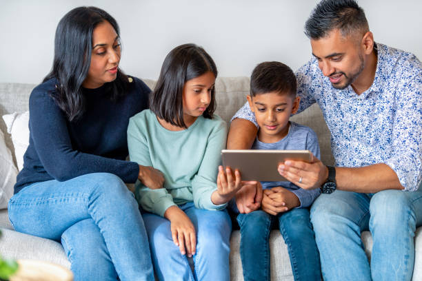 happy family with mother father and 2 children looking at, using and sharing a digital tablet on the sofa - father digital tablet asian ethnicity daughter imagens e fotografias de stock