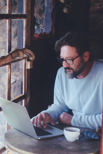 istock Mature man at work on laptop computer sitting at the table inside a home cozy cabin with wooden windows - digital smart working adult people concept lifestyle 1920407382