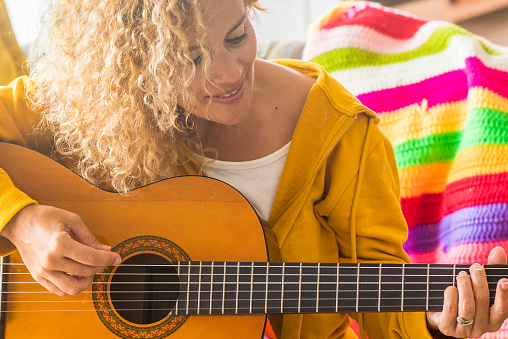 Adult caucasian woman playing acoustic guitar at home sitting on the sofa and smiling with fun - female people with music hobby leisure activity indoor - lady learning to touch guitar cords and enjoy singer lifestyle