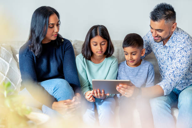 happy family with mother father and 2 children looking at, using and sharing a digital tablet on the sofa - father digital tablet asian ethnicity daughter imagens e fotografias de stock