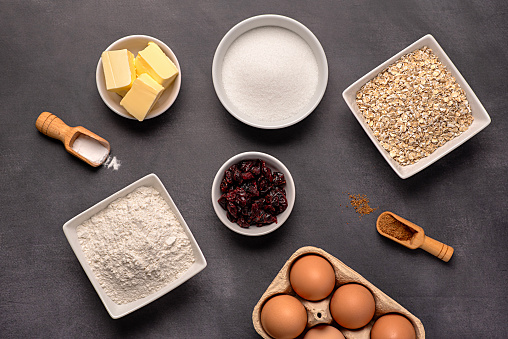 Food photography of raw ingredients of oat biscuits, cookie, dough, egg, sugar, white flour, butter, dried cranberry, vanilla, bake, bakery