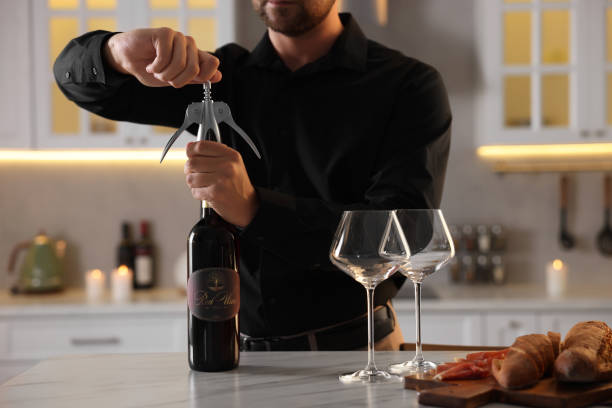 Romantic dinner. Man opening wine bottle with corkscrew at table in kitchen, closeup Romantic dinner. Man opening wine bottle with corkscrew at table in kitchen, closeup uncork wine stock pictures, royalty-free photos & images