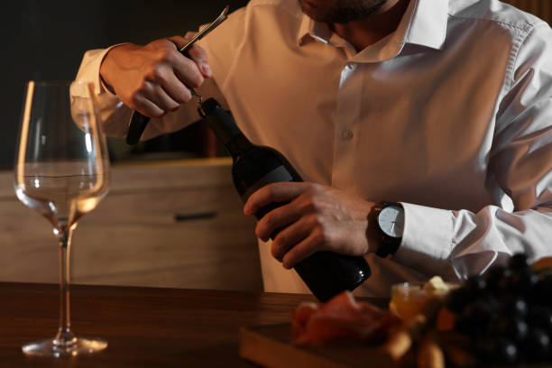 istock Romantic dinner. Man opening wine bottle with corkscrew at table indoors, closeup 1920503087