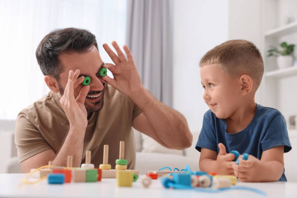 istock Motor skills development. Father and his son playing with wooden pieces and string for threading activity at table indoors 1920530514