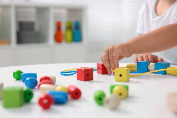 istock Motor skills development. Little boy playing with wooden pieces and string for threading activity at white table indoors, closeup 1920575437