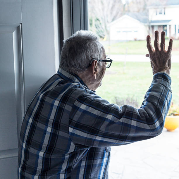 Grandpa Waving Hello or Goodbye Through Glass Front Door A partially deaf Grandpa wearing his hearing aid behind his ear is waving hello or goodbye through his home's glass window front door to off-camera arriving or departing family members or guests after a family holiday gathering. looking out front door stock pictures, royalty-free photos & images
