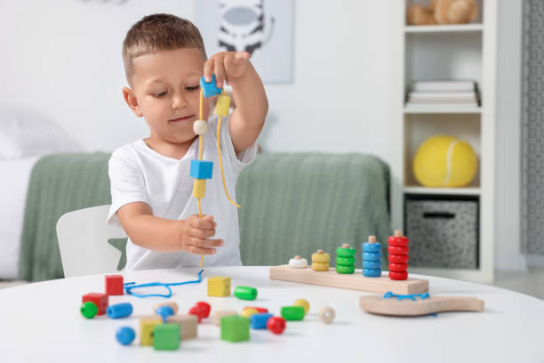 istock Motor skills development. Little boy playing with wooden pieces and string for threading activity at white table indoors 1920577520