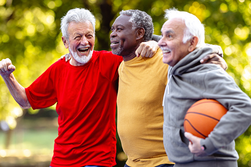 Photo of vital seniors in sports outfits on a basketball court. They are walking and lauging