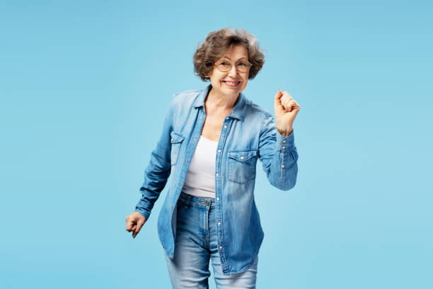 istock Senior smiling woman wearing eyeglasses, dancing looking at camera on blue background, having fun 1920601312