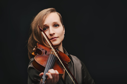 Young violinist woman playing a violin over black background