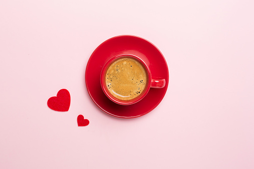 Red cup of coffee with hearts on color background, top view