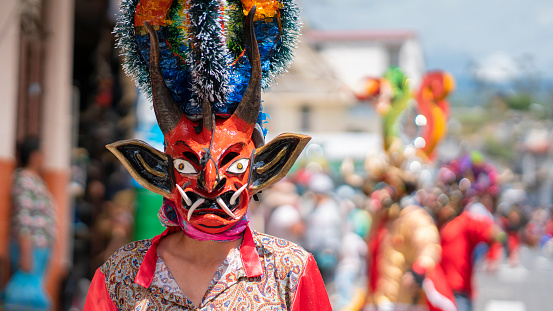 Pillaro, Tungurahua / Ecuador - January 5 2024: Man dressed as a red devil in the foreground with devils dancing in the background out of focus at the Diablada Pillarena parade in the city of Pillaro - Ecuador