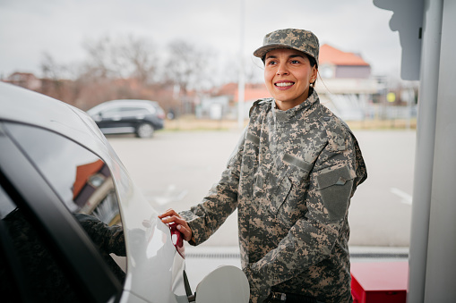 Young Female Military Officer pouring some gas into the car