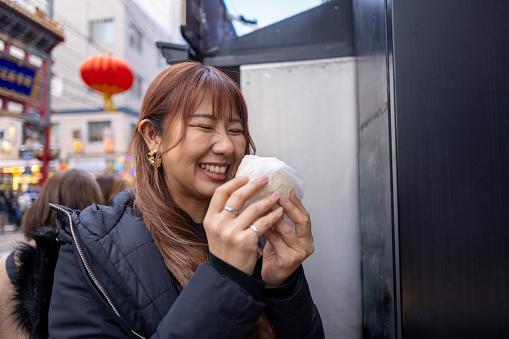 Woman eating “Nikuman” steamed pork bun on street in China town