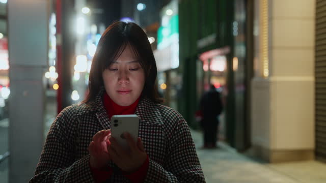 Woman using her smart phone in city at night
