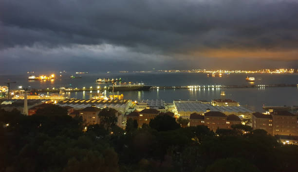 Late evening view of part of Gibraltar, looking over the Alameda gardens towards HM Dockland Gibraltar, over the tankers and other shops crossing the Bay of Gibraltar, and towards the city of Algeciras in Spain in the background.