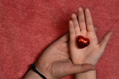 two hands adult and child hand, child holding a red heart chocolate, love concept