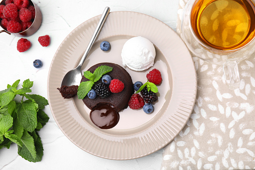 Delicious chocolate fondant served with fresh berries and ice cream on white table, flat lay