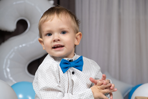 Portrait of a little blond boy with blue eyes wearing a shirt with a bow tie.