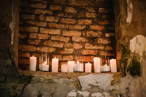 Candles burning near the old stone brick wall. Burning candles in vases on a dark background. Space for text. Dark decor in rustic style. Closeup