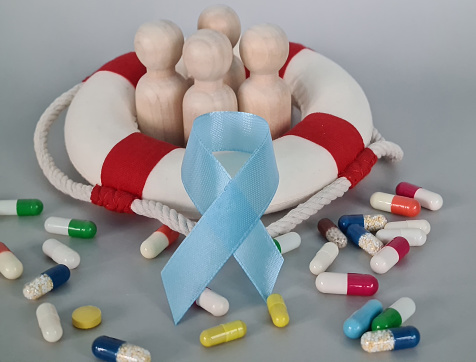 Blue ribbon with little men in lifebuoy and pills. Prostate cancer concept and treatment and health protection