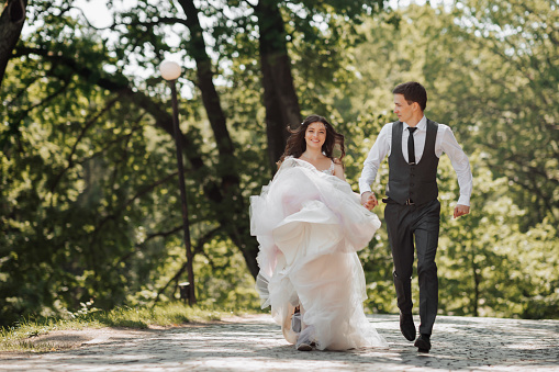 Groom and bride in the garden. Spring wedding in the park. Happy wedding couple running in the park. Stylish and beautiful. Princess dress.