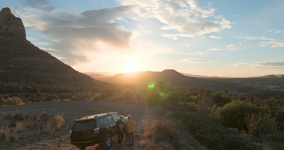 Aerial view of couple and vehicle in red rock desert lands at sunset