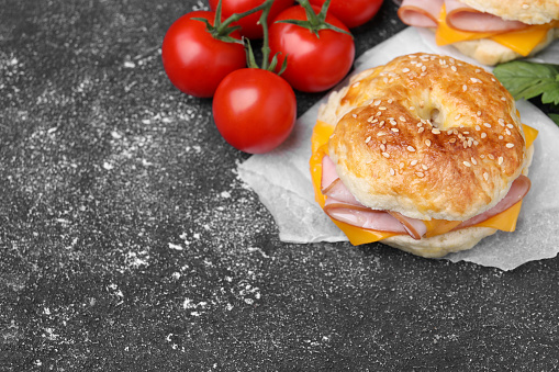 Delicious bagels with ham, cheese and products on dark grey textured table, space for text