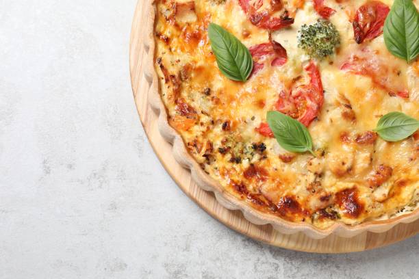 istock Tasty quiche with cheese, tomatoes and basil leaves on light grey table, top view. Space for text 1920922921