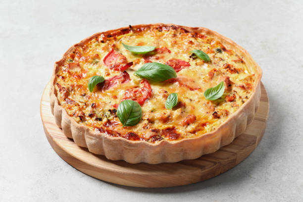 istock Tasty quiche with cheese, tomatoes and basil leaves on light grey table 1920923457