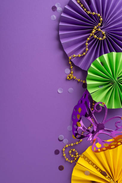 istock Fiesta Fantasy Feast: captivating vertical overhead composition featuring butterfly carnival mask, ornate beads, confetti, paper fans on enchanting purple surface, inviting your text or promo content 1920924530