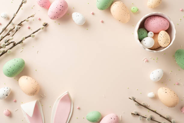 istock Celebrate Easter with this tender top view display. Bowl with color-packed eggs, whimsical bunny ears, pussy-willow twigs, sprinkles form cheerful ensemble on soft beigeâideal for your custom message 1920924541