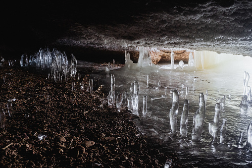 An ice cave, a view inside an underground grotto, frozen icicles, stalagmites, frozen water. A narrow crack in the mountain. The light is in the messenger of the tunnel. High quality photo