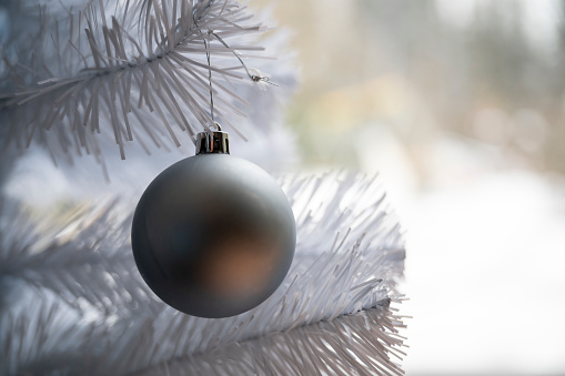 Simple elegant blue christmas bauble hanging on a white holiday tree.