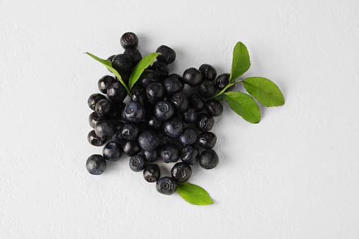 Pile of ripe bilberries and leaves on white background, flat lay