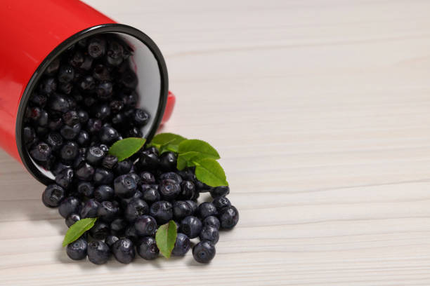 istock Mug with ripe bilberries on white wooden table, closeup. Space for text 1920941919