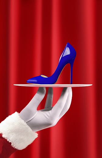Santa holding a chic women shoe with high heels in front of a red curtain