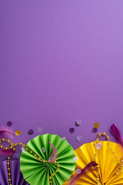 istock Whimsical Carnival Whirl: Mesmerizing vertical top view of glamorous beads, feathers, confetti, and dynamic paper fans arranged on vibrant purple background, with an open space for your text or advert 1920948834